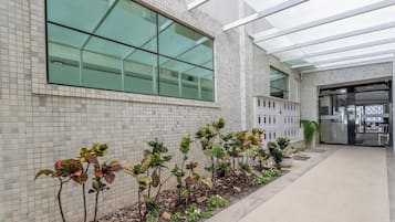 Un edificio moderno con fachada de baldosas, entrada de vidrio y un sendero bordeado de plantas.