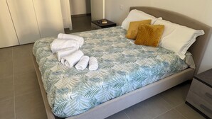 A bed with a leaf-patterned bedspread, two pillows, and rolled towels.