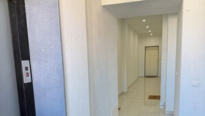 A hallway with a door, a light switch, and a tiled floor.