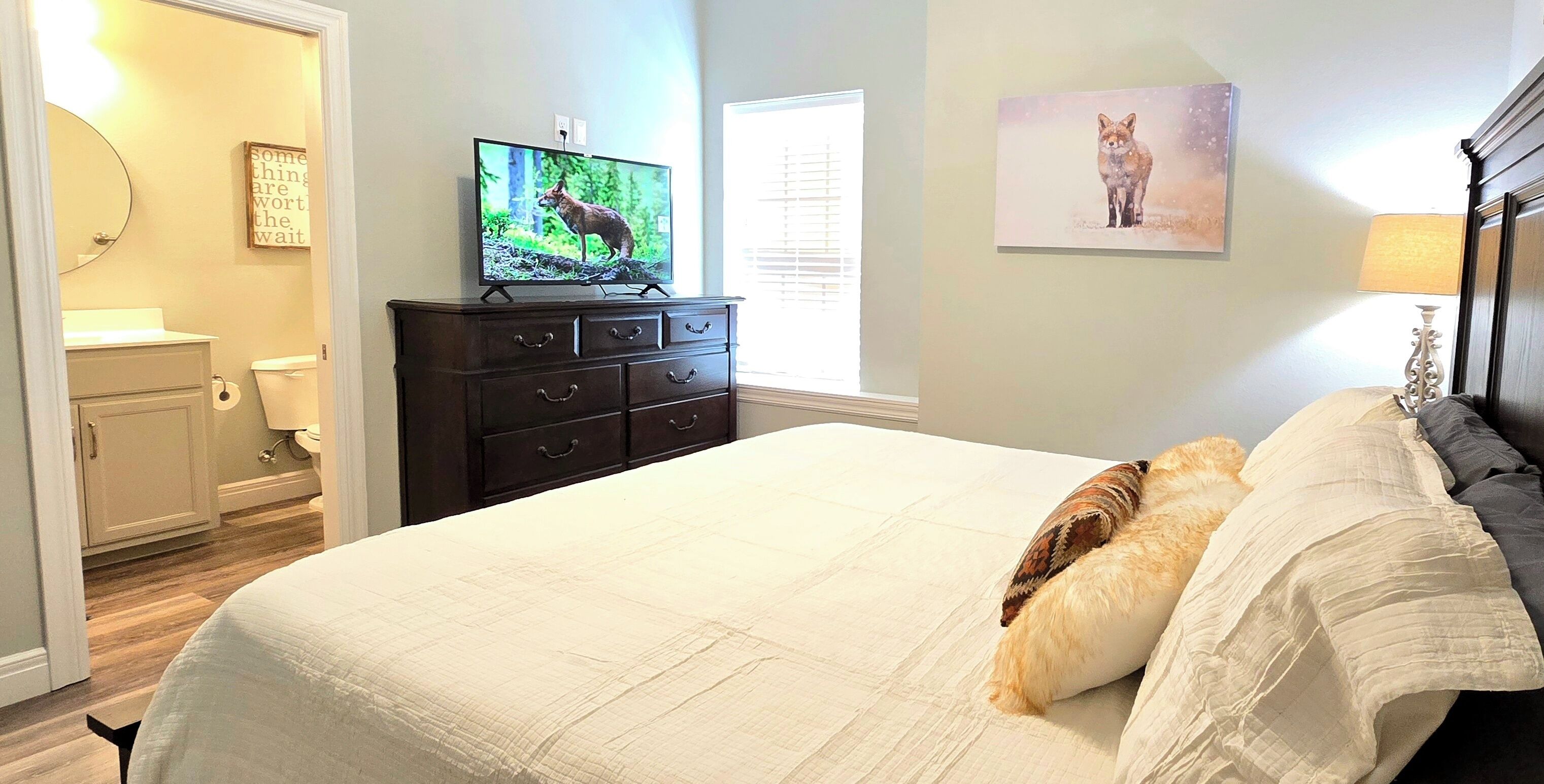 A bedroom with a bed, a dresser, a television, a window, and a painting on the wall.