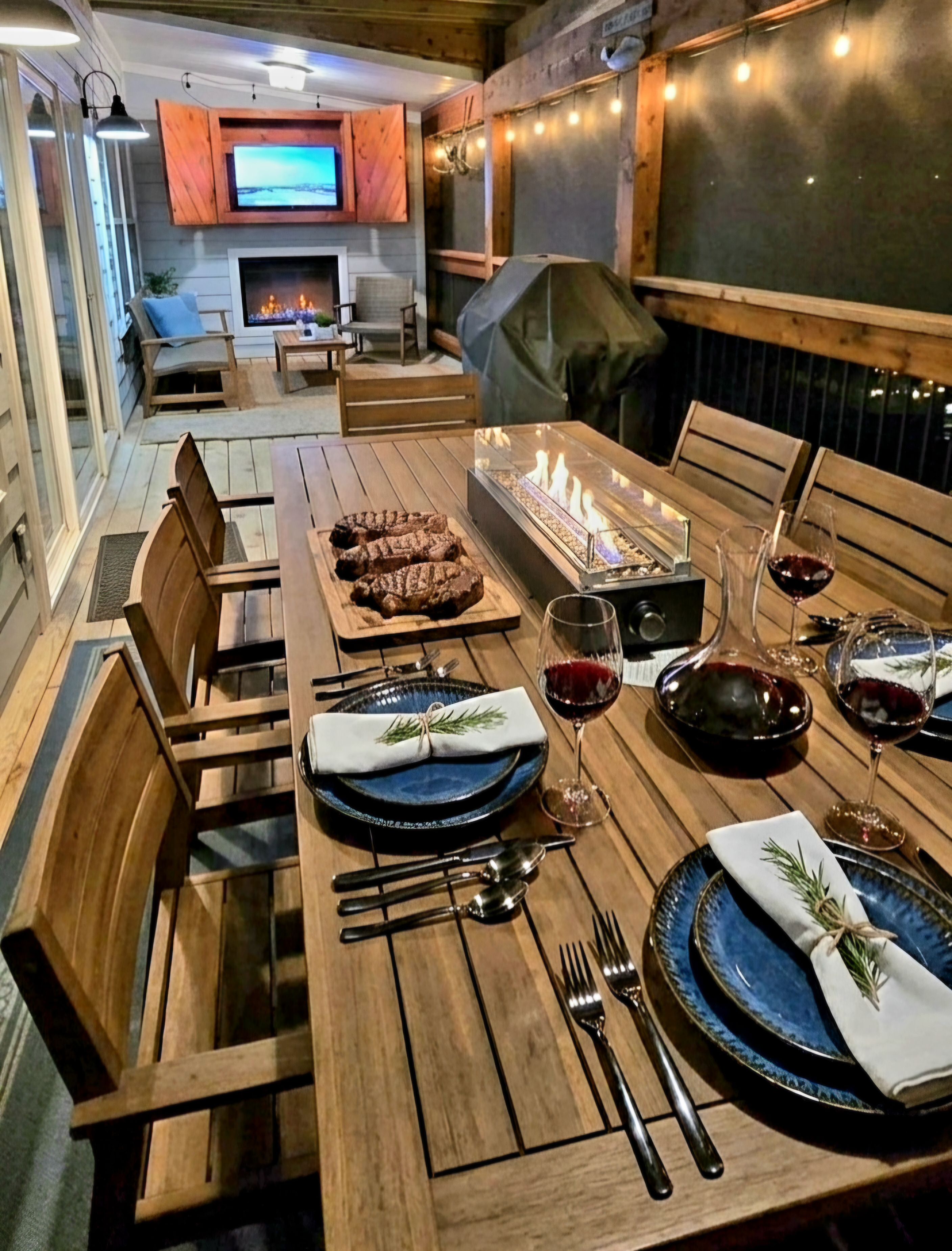 Un comedor con una mesa de madera preparada para dos personas, una chimenea y un televisor al fondo.