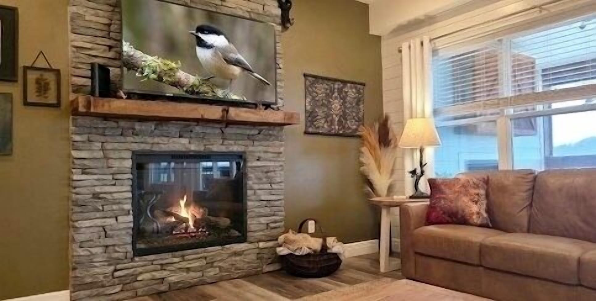 A stone fireplace with a fire, a couch, and a window with blinds.