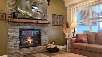A stone fireplace with a fire, a couch, and a window with blinds.
