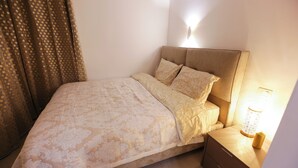 Un letto rifatto con precisione, con una coperta e dei cuscini a fantasia, un comodino con una lampada e una tenda a pois.