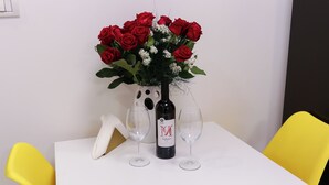 Un tavolo con un vaso di rose rosse, una bottiglia di vino e due bicchieri da vino.
