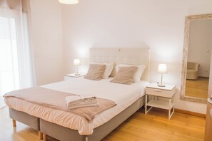 A neatly made bed with a headboard, two bedside tables with lamps, and a large mirror on the wall.