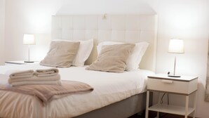 Un lit bien fait, avec deux oreillers, une table de chevet avec une lampe et une petite étagère.