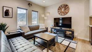 A modern living room with a large TV, leather sofas, a coffee table, and a large clock on the wall.