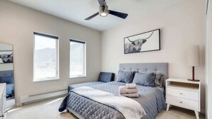 A bedroom with a bed, a nightstand, a ceiling fan, and two windows.