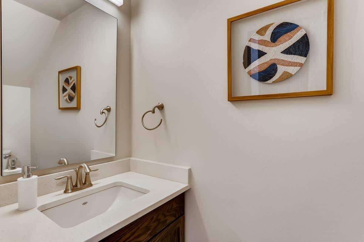 Un baño con un lavamanos blanco, un espejo y dos anillas para toallas en la pared.
