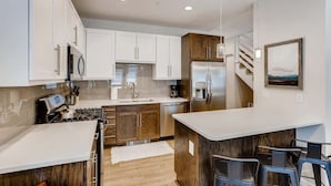 A modern kitchen with white cabinets, a stainless steel refrigerator, and a wooden island. - Trekker Townhome | Mountain Charm | New Floors! (Georgetown)