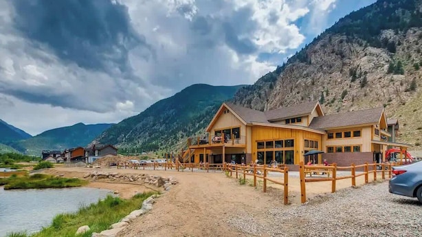 A lodge with a wooden exterior, a covered outdoor seating area, and a view of a mountain range. - Trekker Townhome | Mountain Charm | New Floors! (Georgetown)