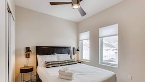 A bedroom with a bed, a standing lamp, a ceiling fan, and two windows. - Trekker Townhome | Mountain Charm | New Floors! (Georgetown)