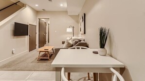 Un salon moderne avec une table blanche, un canapé, un téléviseur fixé au mur et un escalier menant à une autre pièce.