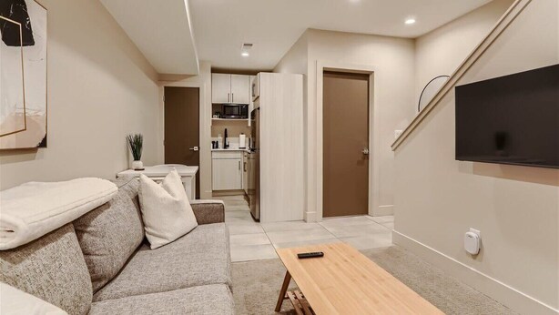 Un salon moderne avec un canapé, une table basse, un téléviseur fixé au mur et un coin cuisine à l’arrière-plan.