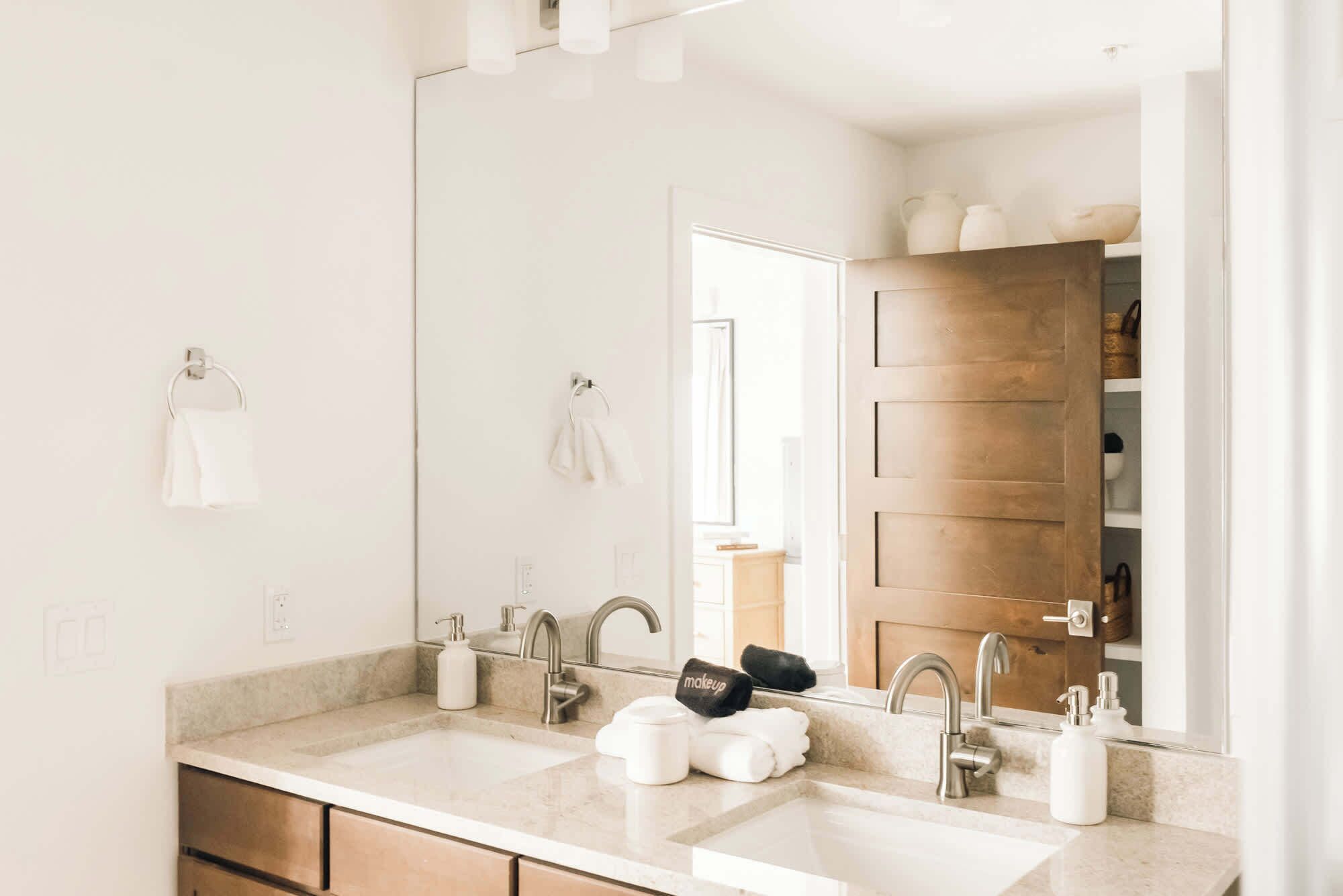 A bathroom with two sinks, a large mirror, and a wooden door in the background.