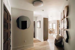 A hallway with a round mirror, a wooden door, and a dining area with a table and chairs. - Refined Riverfront Living - King Suite & Views (Silverthorne)