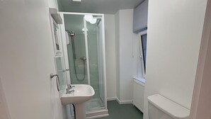 A compact bathroom with a toilet, sink, and glass-enclosed shower. - Glendale Guesthouse (Oban)