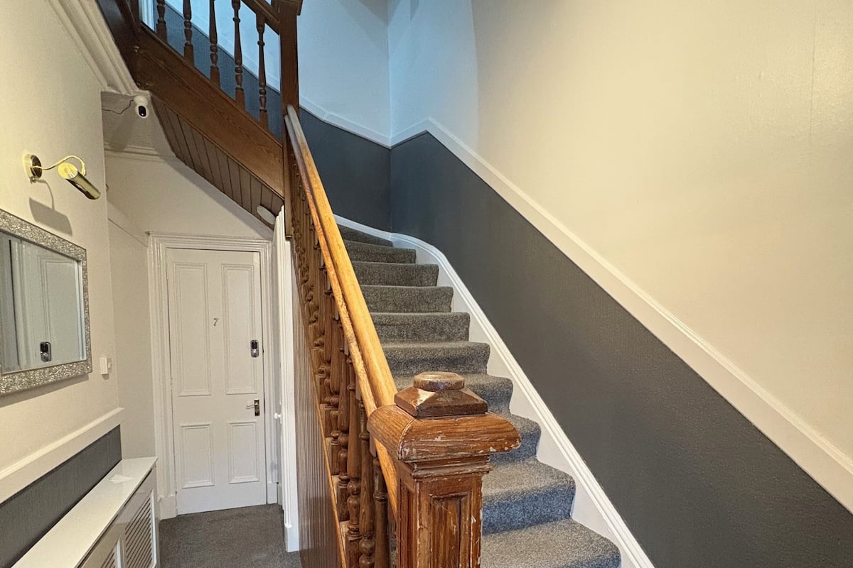 A staircase with wooden handrails and carpeted steps, leading to a landing with a white door and a mirror on the wall.