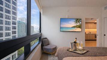 Une chambre d’hôtel moderne dotée d’une grande fenêtre, d’un lit, d’un petit coin salon, d’une télévision et offrant une vue sur la plage.