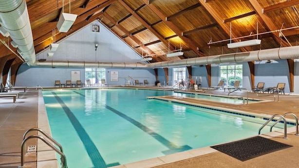 Ein Hallenbad mit hoher Holzbalkendecke, klarem Poolbereich und Liegestühlen.