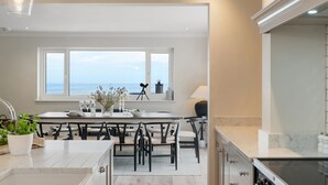 A modern kitchen with a large window, a dining area with chairs, and a view of the sea. - Luxury seaside home | 5 mins from beach | sea view | hot tub (Downderry)