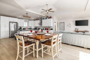A modern kitchen with white cabinets, a wooden dining table, and a ceiling fan. - Beachfront House w/ Patio BBQ & Fire Pit (Carlsbad)