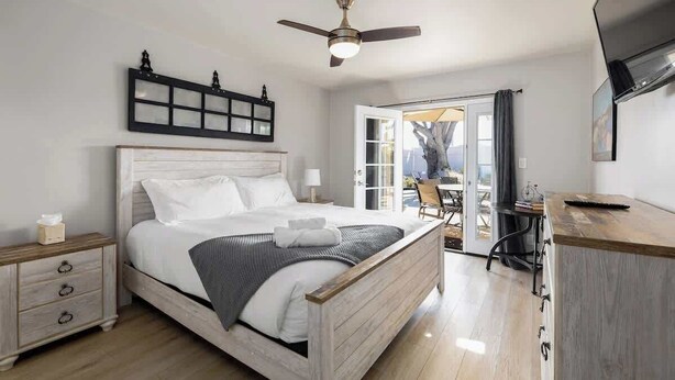 Ein Schlafzimmer mit Bett, Nachttisch, Schreibtisch, Deckenventilator und Blick durch eine Glast ür.