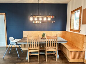 A dining area with a wooden table, chairs, and a bench. There is a wall-mounted light fixture above the table. - Family-Friendly Luxury Cabin SLIDE+SWINGSET+Movie Room - Hot Tub & Mountain View (Piercetown)