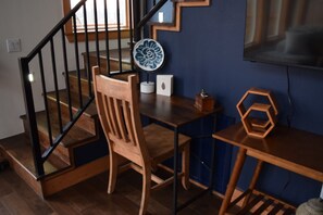 Eine Treppe mit Holzstufen und schwarzen Geländern, ein Holzstuhl, ein kleiner Tisch mit einem blauen Keramikteller und ein hexagonales Holzobjekt auf einem Tisch.
