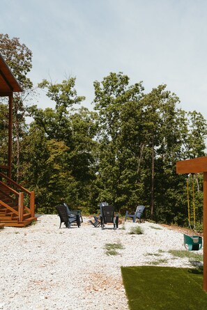 A wooden deck with outdoor seating, surrounded by trees and a grassy area. - Family-Friendly Luxury Cabin SLIDE+SWINGSET+Movie Room - Hot Tub & Mountain View (Piercetown)