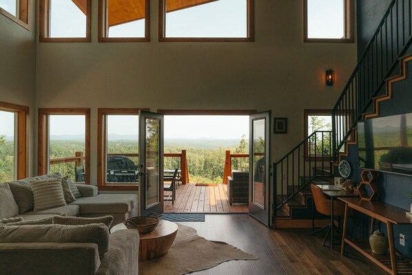 A spacious living room with a large sofa, a coffee table, and a view of the outdoors through large windows. - Family-Friendly Luxury Cabin SLIDE+SWINGSET+Movie Room - Hot Tub & Mountain View (Piercetown)