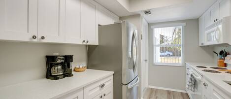 A modern kitchen with white cabinets, a stainless steel refrigerator, a coffee maker, and a window providing a view of the outside.