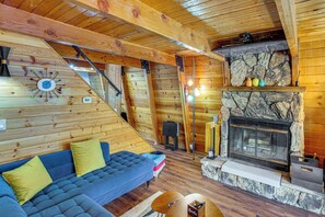 Ein gemütliches Blockhaushaus-Interieur mit Kamin aus Stein, Holzwänden, einem blauen Sofa und einer Treppe.