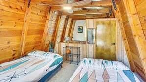 Una camera da letto mansardata accogliente con due letti, una ventola a soffitto, un angolo cottura e una porta in legno.