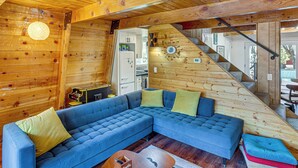 Interno di una baita con un divano componibile blu, una scala in legno e un angolo cucina.