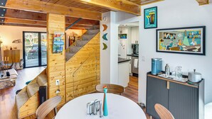 Un interno moderno con una scala in legno, una zona pranzo con tavolo bianco e una cucina sullo sfondo.