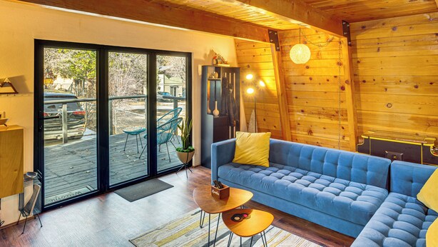 Un interno moderno in stile baita con un divano blu, pareti in legno e una porta vetrata che dà su un patio esterno.