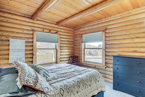 Un dormitorio de cabaña de troncos con cama, cómoda y ventanas.