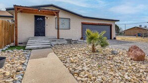 A single-story house with a garage, a covered entryway, and a small palm tree in the front yard. - Fully Renovated, Near NMSU! Convenient Family Home (Las Cruces)