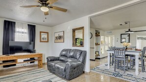 A living room with a leather sofa, a wooden coffee table, a flat-screen TV, and a ceiling fan. - Fully Renovated, Near NMSU! Convenient Family Home (Las Cruces)