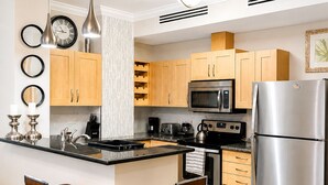 A modern kitchen with a central island, stainless steel appliances, wooden cabinets, and two bar stools. - Exquisite One-bedroom Condo • City View • Port of Spain • Modern • Vibrant • (Port of Spain)