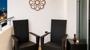 A balcony with two wicker chairs, a small table, a decorative wall piece, and a lantern. - Exquisite One-bedroom Condo • City View • Port of Spain • Modern • Vibrant • (Port of Spain)
