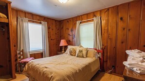 A bedroom with a bed, a chair, a lamp, and a wooden wardrobe.