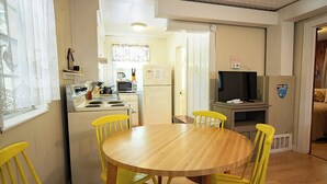 A compact kitchen with a dining table and chairs, a refrigerator, microwave, and a television.