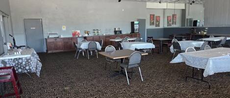 A spacious indoor area with multiple tables and chairs, a counter with a coffee machine, and a patterned carpet.