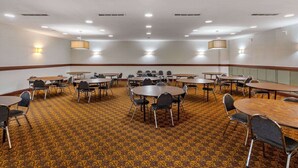 A conference room with multiple tables and chairs, carpeted floor, and ceiling lights.