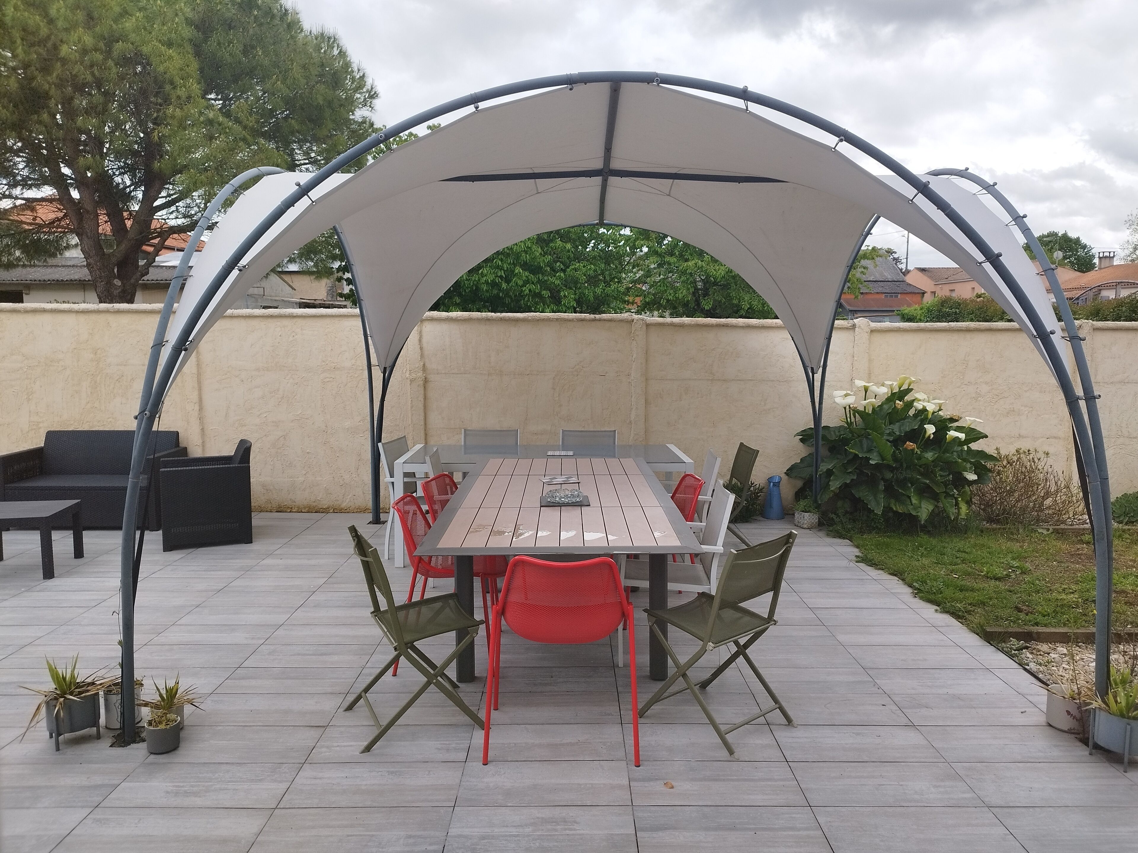 An outdoor patio with a covered dining area, including a table and chairs, surrounded by potted plants and a wall.