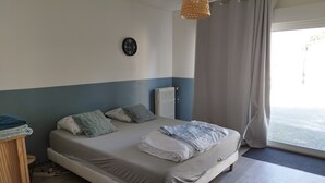 Una camera da letto con un letto, cuscini, una sveglia, un termosifone, una finestra con tende e un comodino in legno.
