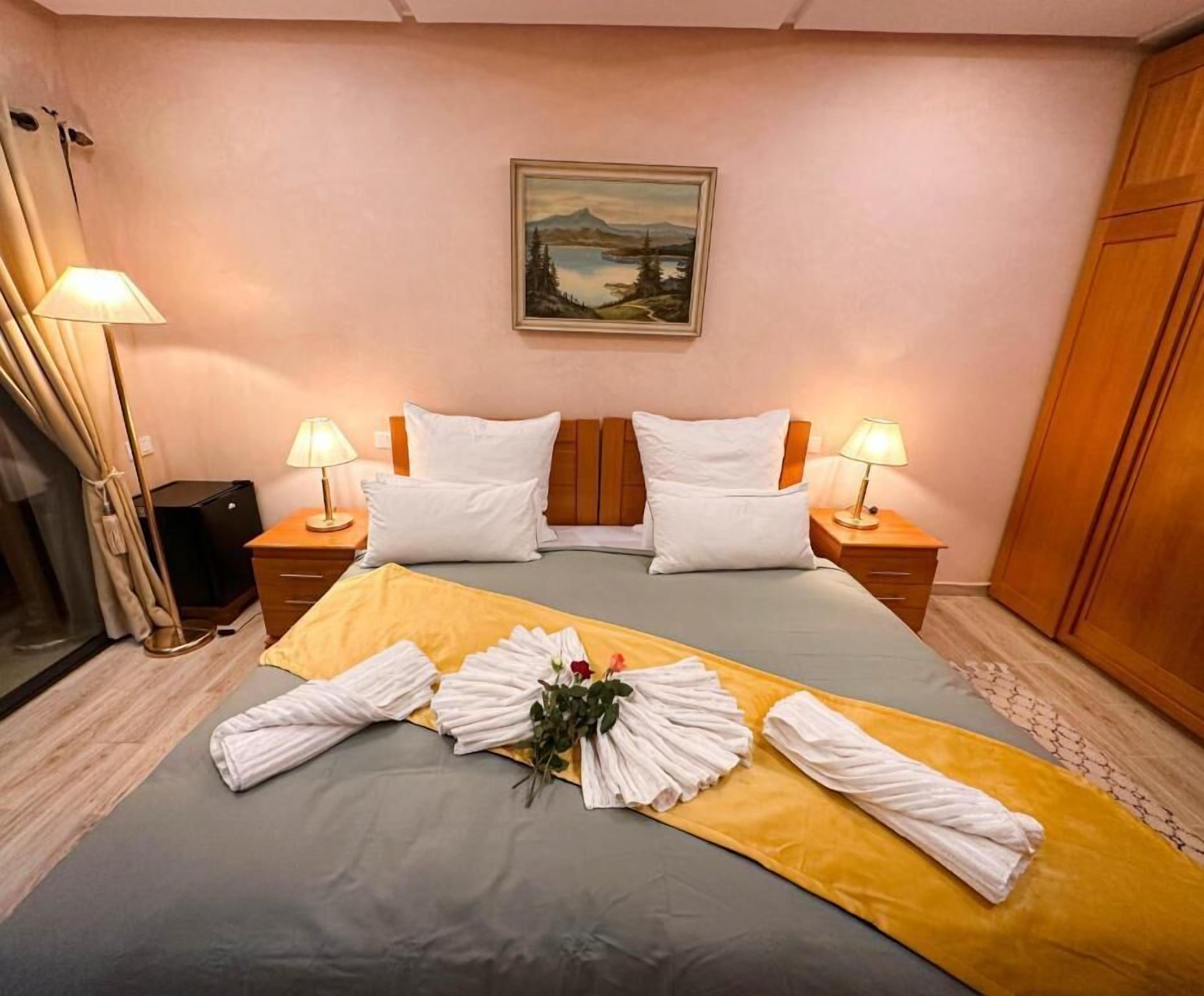 Une chambre d’hôtel avec un lit, deux lampes de chevet, un tableau au mur et une armoire en bois.